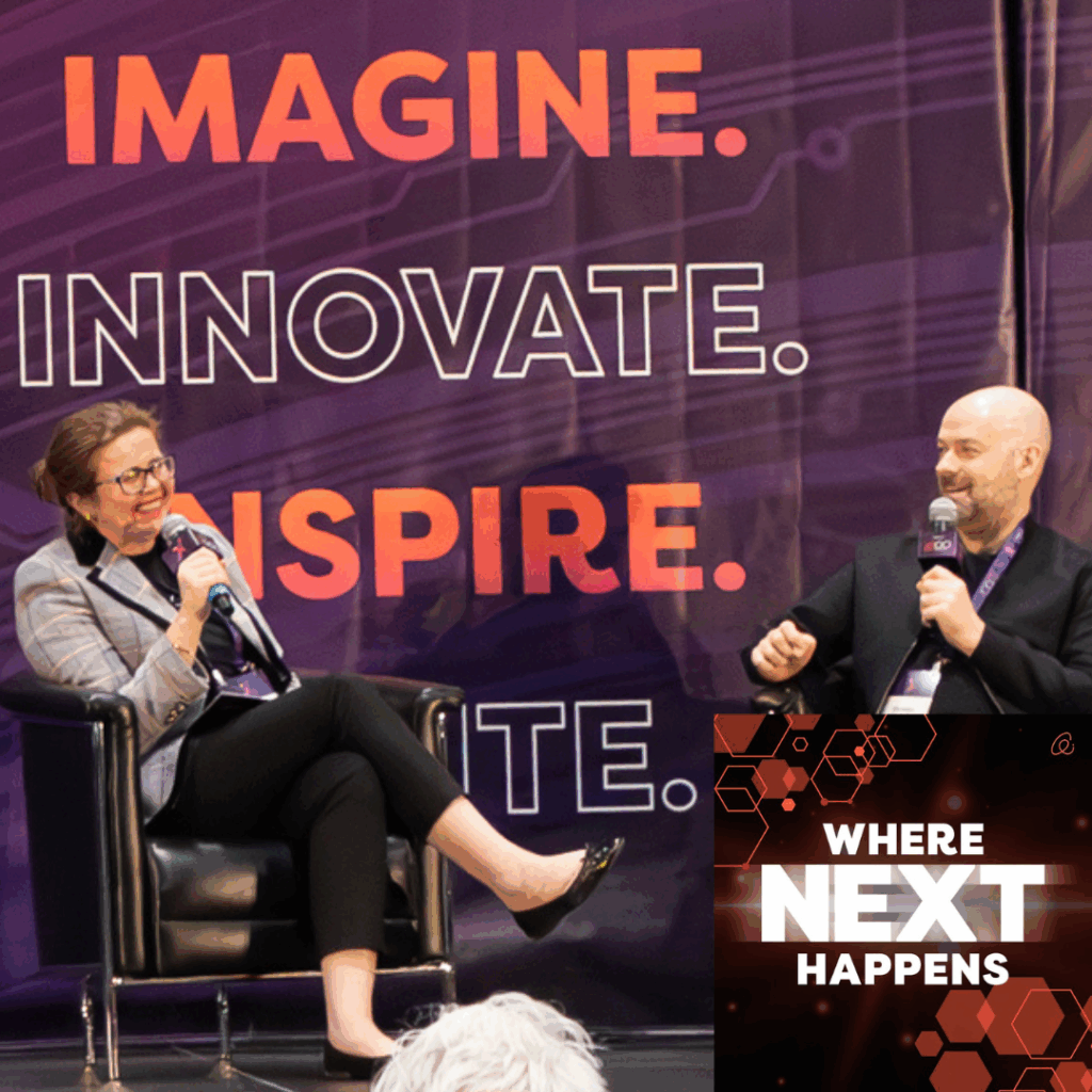 Two speakers seated on stage hold microphones during a panel discussion, with large backdrop text reading “IMAGINE. INNOVATE. INSPIRE.” and a graphic overlay reading “WHERE NEXT HAPPENS.”